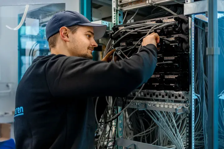 En tekniker jobber med kabler i et serverrom.