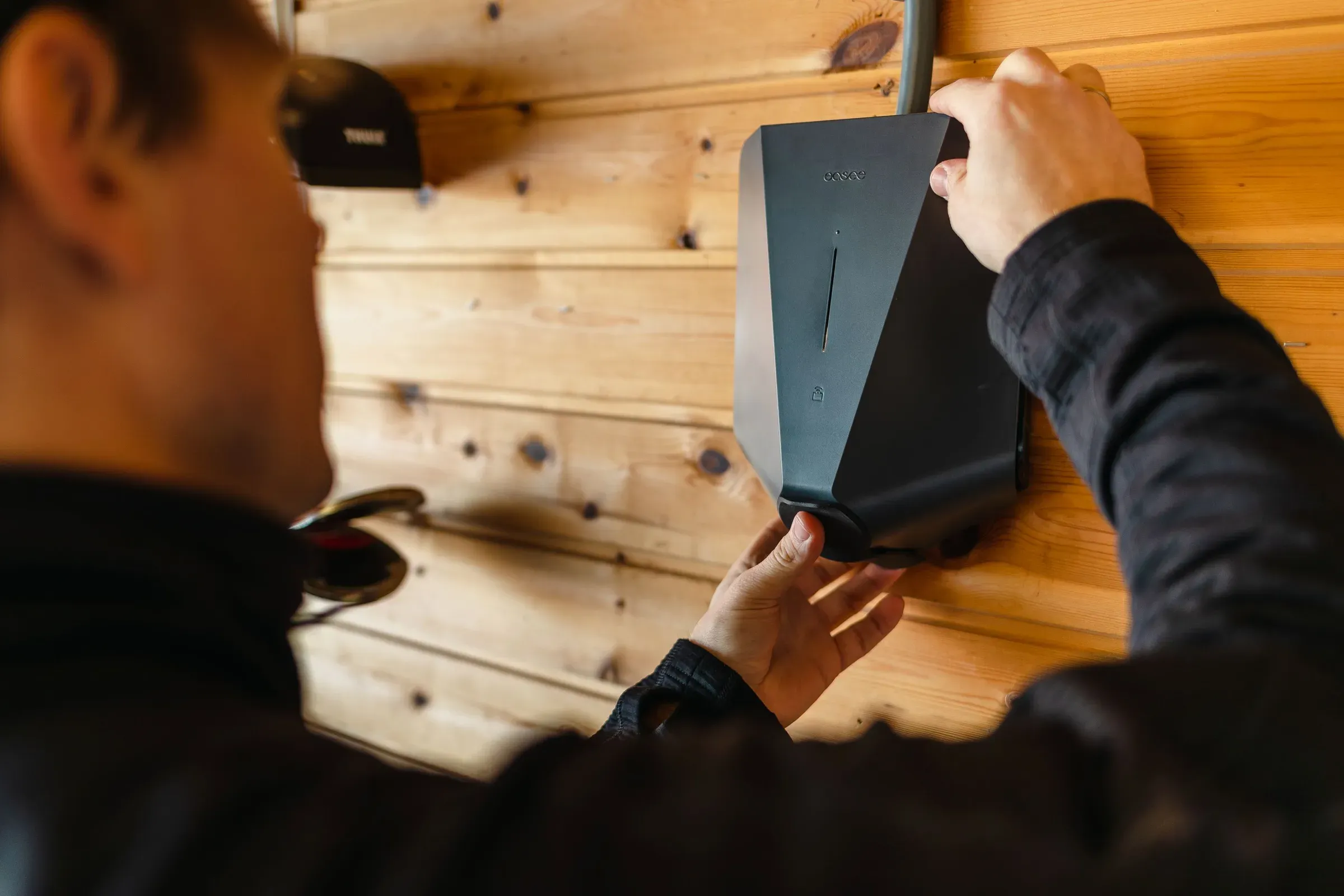 En person installerer en elektrisk enhet på en vegg av trepanel.