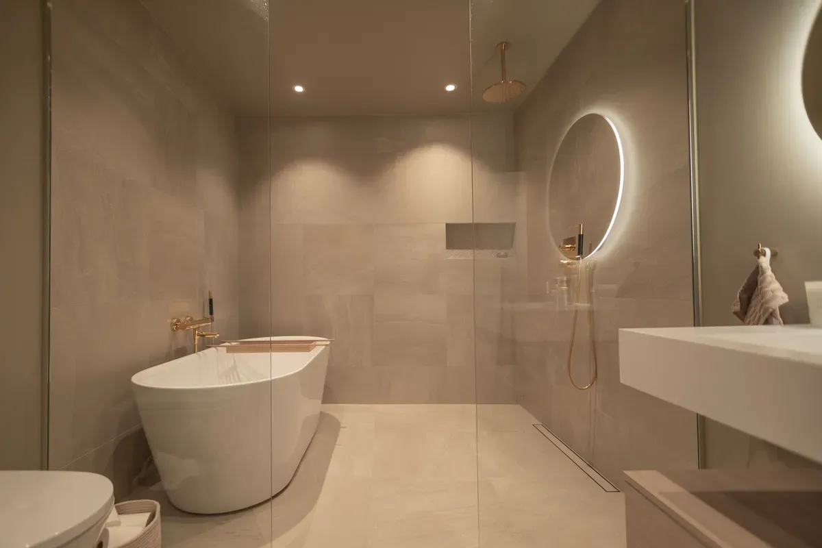 Moderne bad med frittstående badekar, rund speil med lys, dusj og minimalistisk interiør.