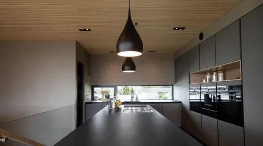 Moderne kjøkken med minimalistisk design, grå innredning, stor kjøkkenøy og hengende svarte lamper.