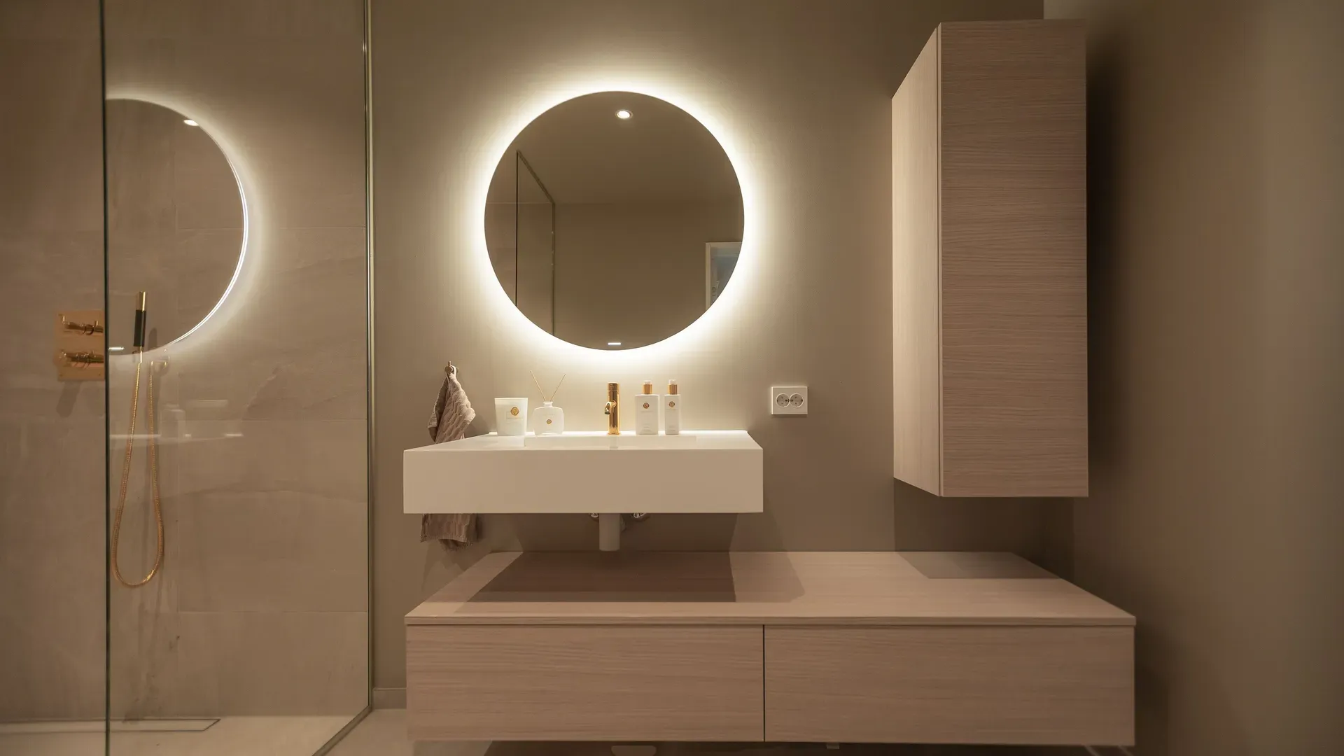 Moderne baderom med runde, belyste speil, minimalistisk servant og lyst treverk på skapene.