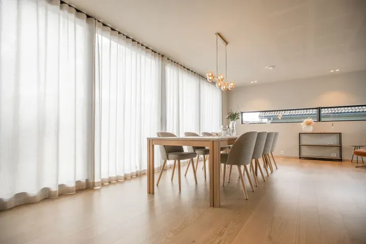 Lyst og moderne spisestue med stort vindu, gardiner, spisebord, seks stoler, og minimalistisk innredning.