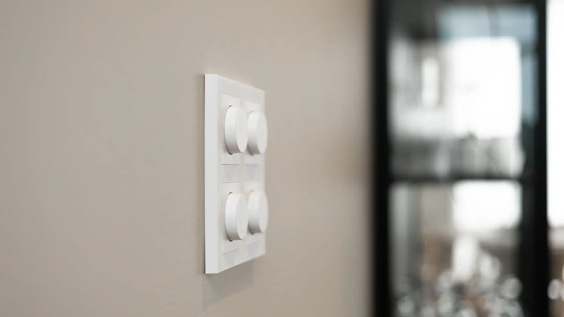 Fire hvite dimmerbrytere montert på en lys vegg, med uklart skap i bakgrunnen.