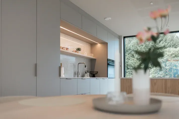 Moderne kjøkken med grå skap, innebygd ovn og vask, med en uskarp blomst i forgrunnen.