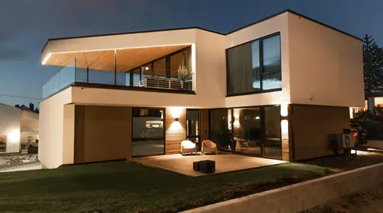 Moderne tomannsbolig med store vinduer og uterom, fotografert om kvelden med utelys på.