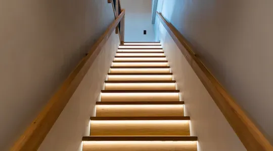 Innendørs trapp med tretrinn og LED-belysning under hvert trinn, sett fra bunnen av trappen.