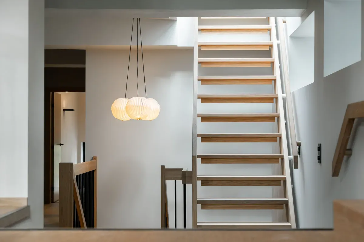 Moderne trappeoppgang i et lyst, minimalistisk interiør med tretrapp og hengende lamper.