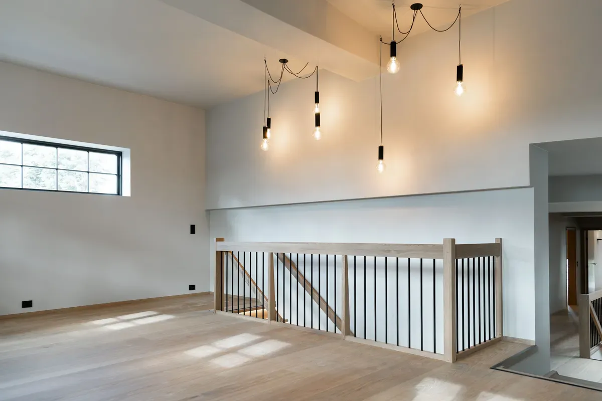 Moderne og lys loftsetasje med parkettgulv, hengende lyspærer og rekkverk av tre og svart metall.