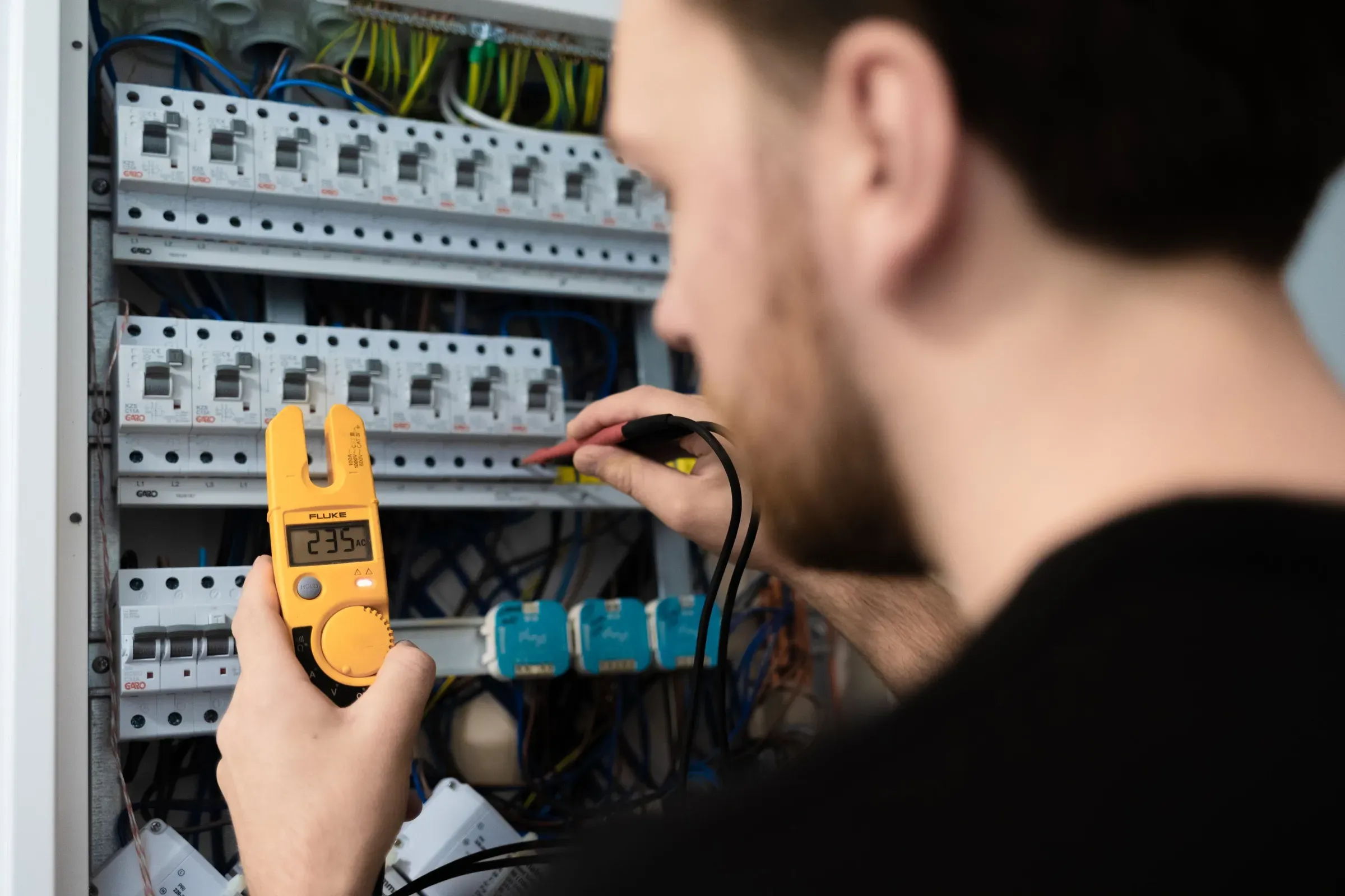 En person tester spenningen i et sikringsskap med et digitalt multimeter.