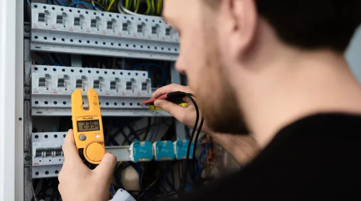 En person tester spenningen i et sikringsskap med et digitalt multimeter.