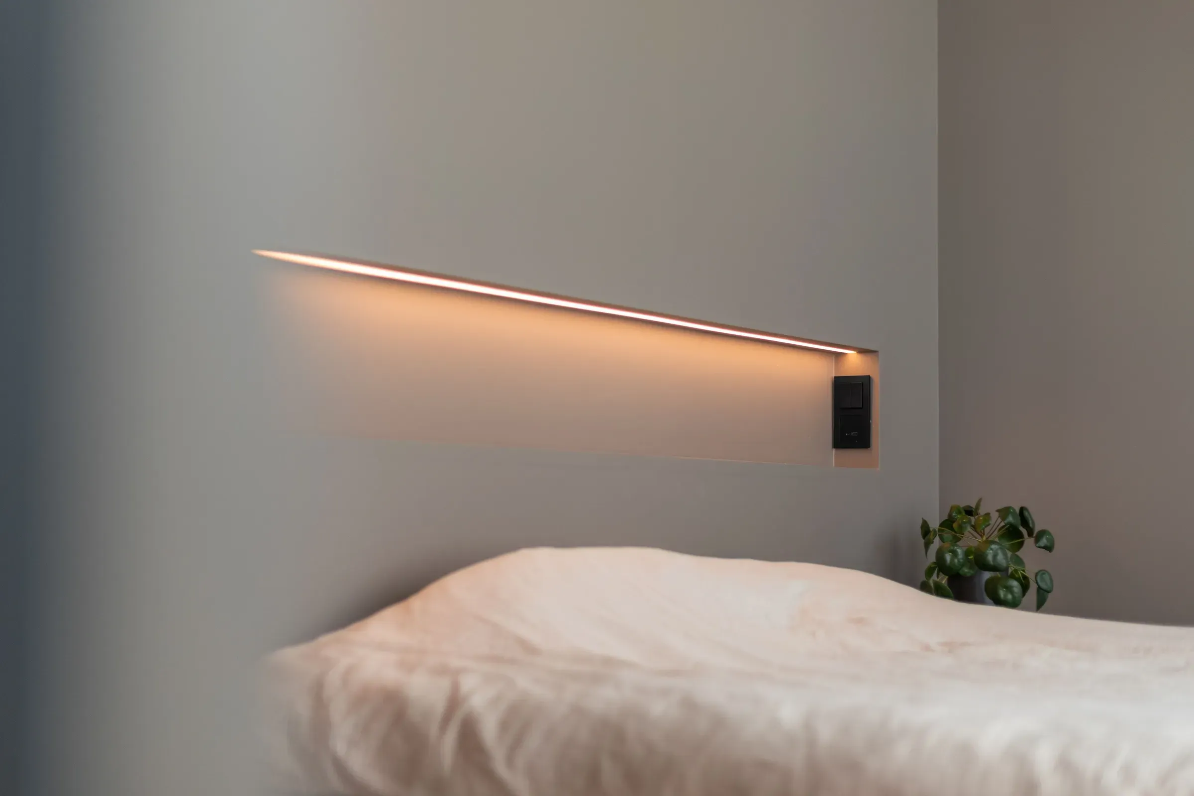 Minimalistisk soverom med en seng, en lang LED-lysstripe på veggen og en grønn plante.