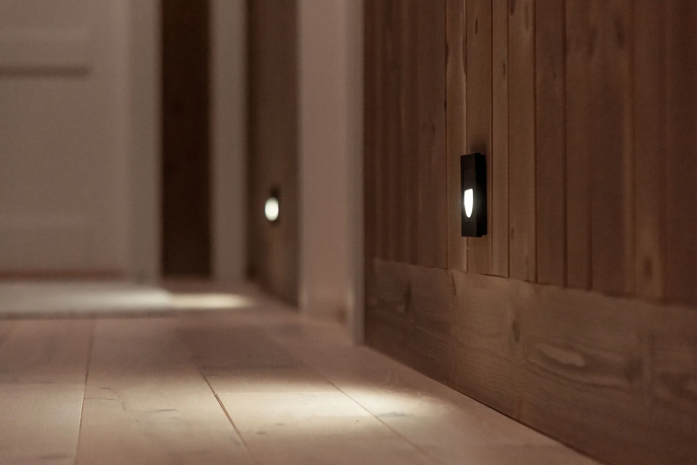 Nærbilde av en gang med nattbelysning montert lavt på tredetaljert vegg.