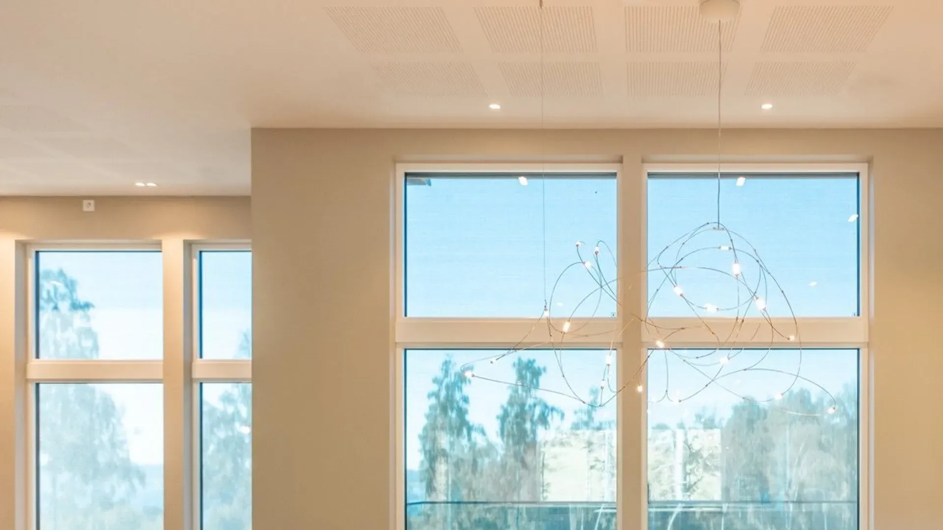 Store vinduer i et lyst rom med utsikt til trær utenfor.