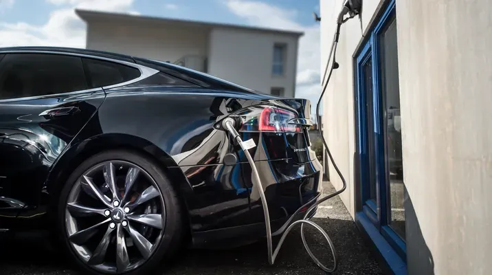 Elektrisk bil som lades via en ladestasjon på en bygning.