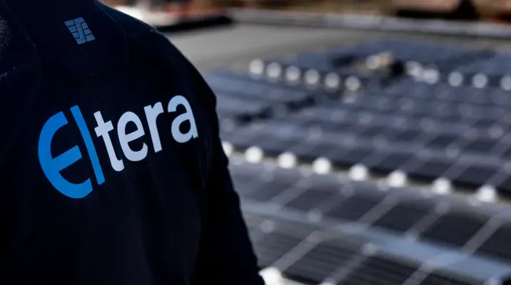 Person iført jakke med Eltera-logoen foran et solcelleanlegg.