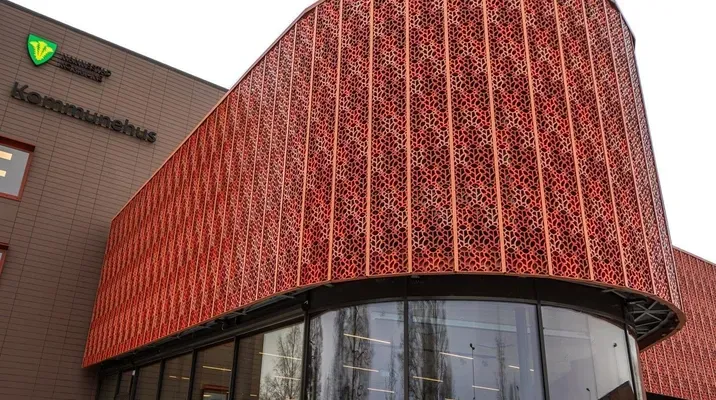 Moderne kommunebygg med rød dekorativ fasade og store vinduer.