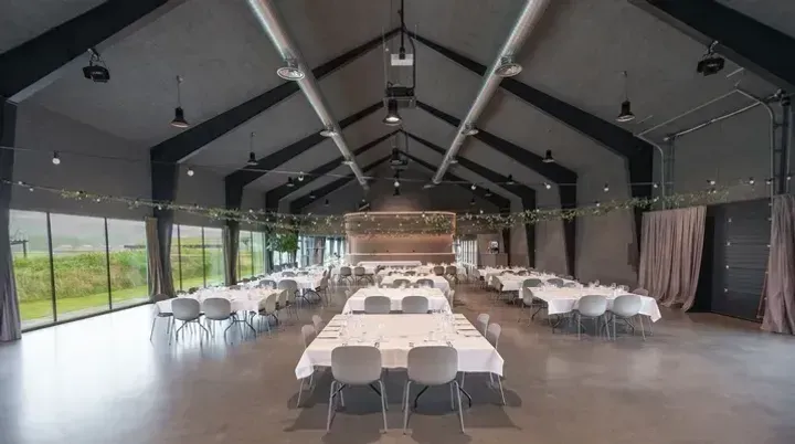 Elegant selskapssal på Solastranden Gård med dekkede bord og grønne dekorasjoner i taket.