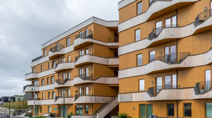 Moderne leilighetsbygg med trepanel og balkonger, sett fra bakkeplan på en overskyet dag.