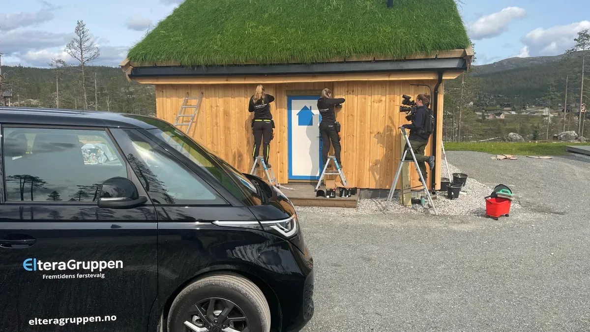 Tre personer jobber på utsiden av en hytte med torvtak. En svart bil med ElteraGruppen-logoen står parkert ved siden av hytta.