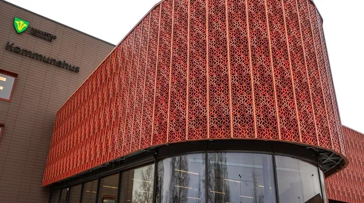 Moderne kommunebygg med rød dekorativ fasade og store vinduer.