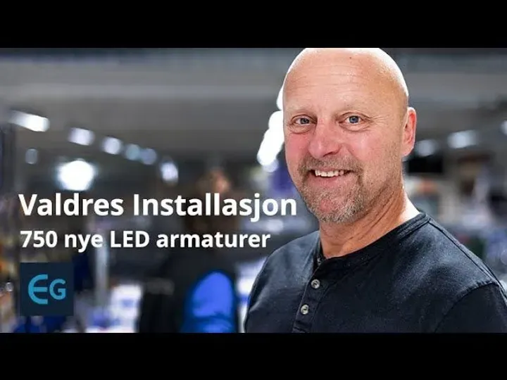 Smilende mann i arbeidsklær står innendørs med teksten 'Valdres Installasjon, 750 nye LED armaturer' over bildet.