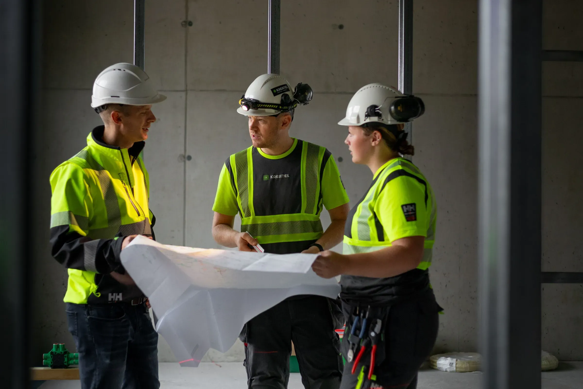 3 kreatel ansatte i verneutstyr som ser på en plantegning