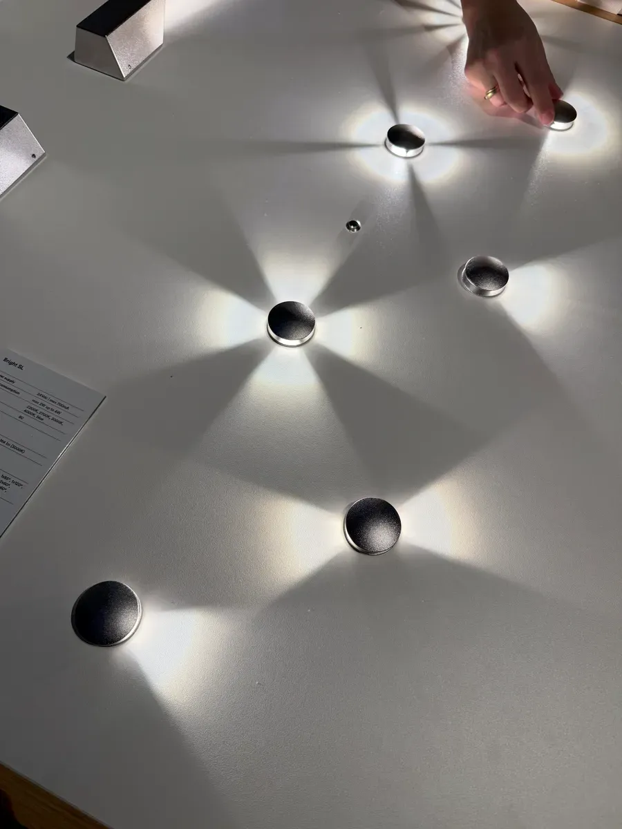 Runde svarte magneter eller objekter plassert på en hvit overflate, omgitt av konsentrerte lysstråler og skygger. En hånd justerer et av objektene øverst til høyre.