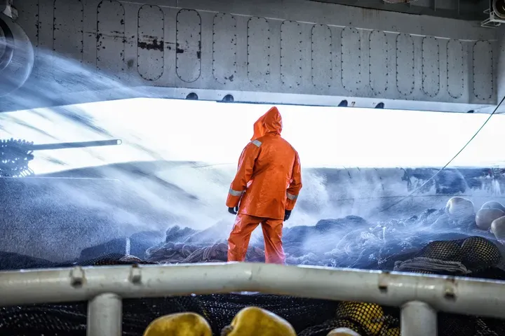 Fisker i orange oljeklede står på fiskebåt i hardt vær_Marint kompetansesenter