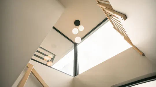 Utsikt oppover fra en trapp med moderne rekkverk, store vinduer og hengende lampe på taket.