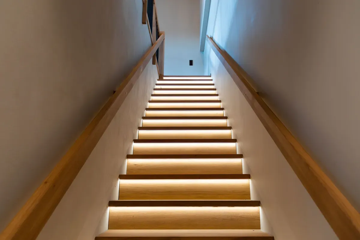 Innendørs trapp med tretrinn og LED-belysning under hvert trinn, sett fra bunnen av trappen.