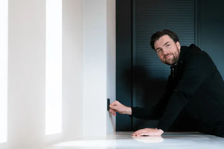 En mann i mørke klær trykker på en lysbryter på en hvit vegg.