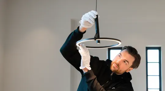 En mann med hvite hansker installerer eller monterer en moderne, ringformet taklampe.