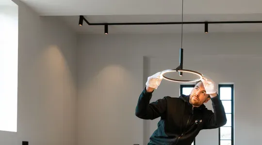 En mann med hvite hansker monterer en rund lampe i taket i et moderne rom.